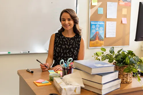Woman seated at a classroom desk with books and supplies
