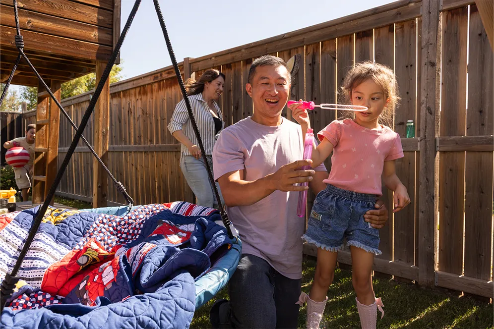 Father and young daughter blowing bubbles together in a backyard