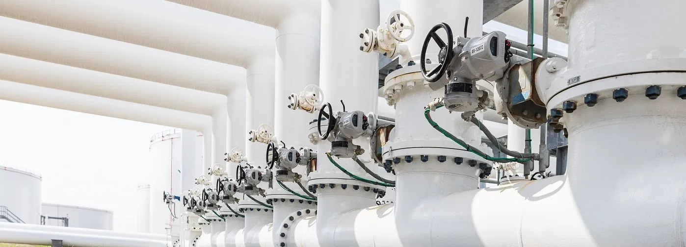 Image of a natural gas facility including white gas pipes, valves, and gas storage containers.